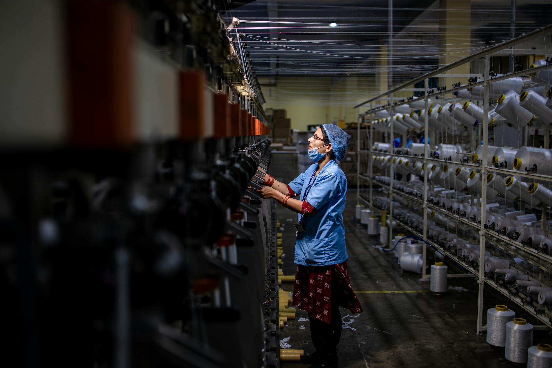 Pracownica obsługuje maszynę włókienniczą w zapylonej hali produkcyjnej