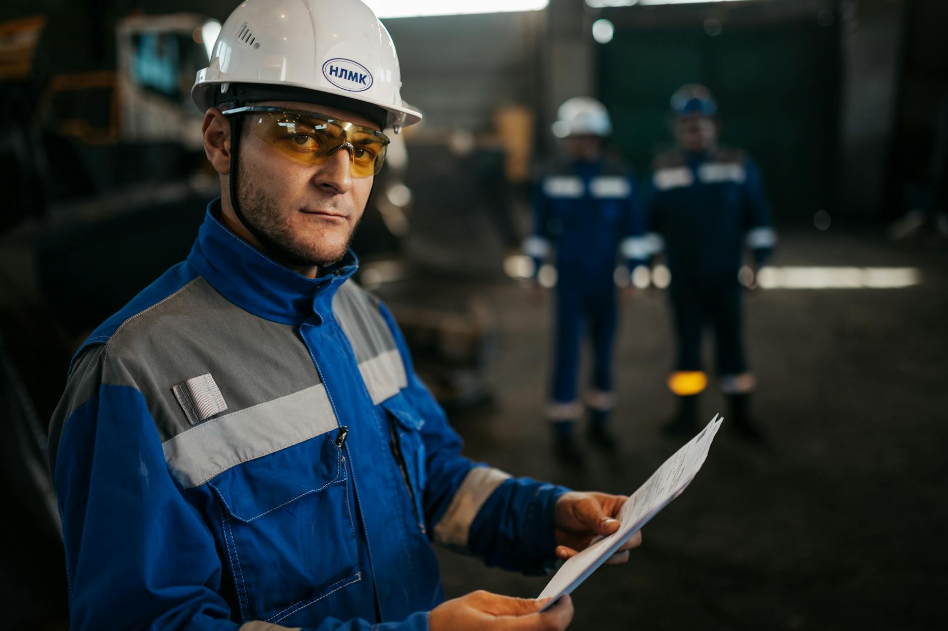 Pracownik w kasku i okularach BHP analizuje dokumenty w hali produkcyjnej