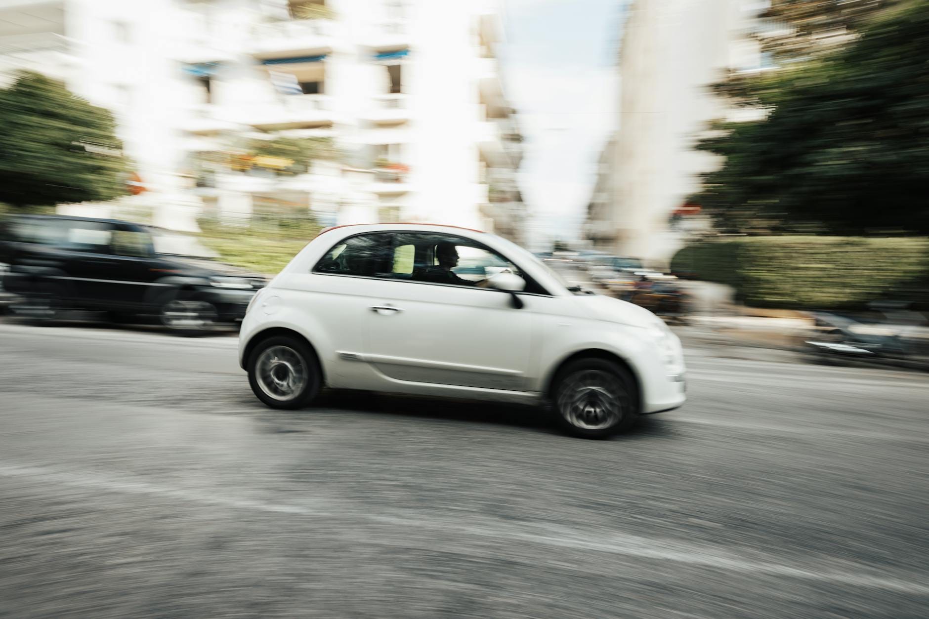 Biała miejska Fiat Panda w ruchu na ulicy, lekko rozmazane tło miasta