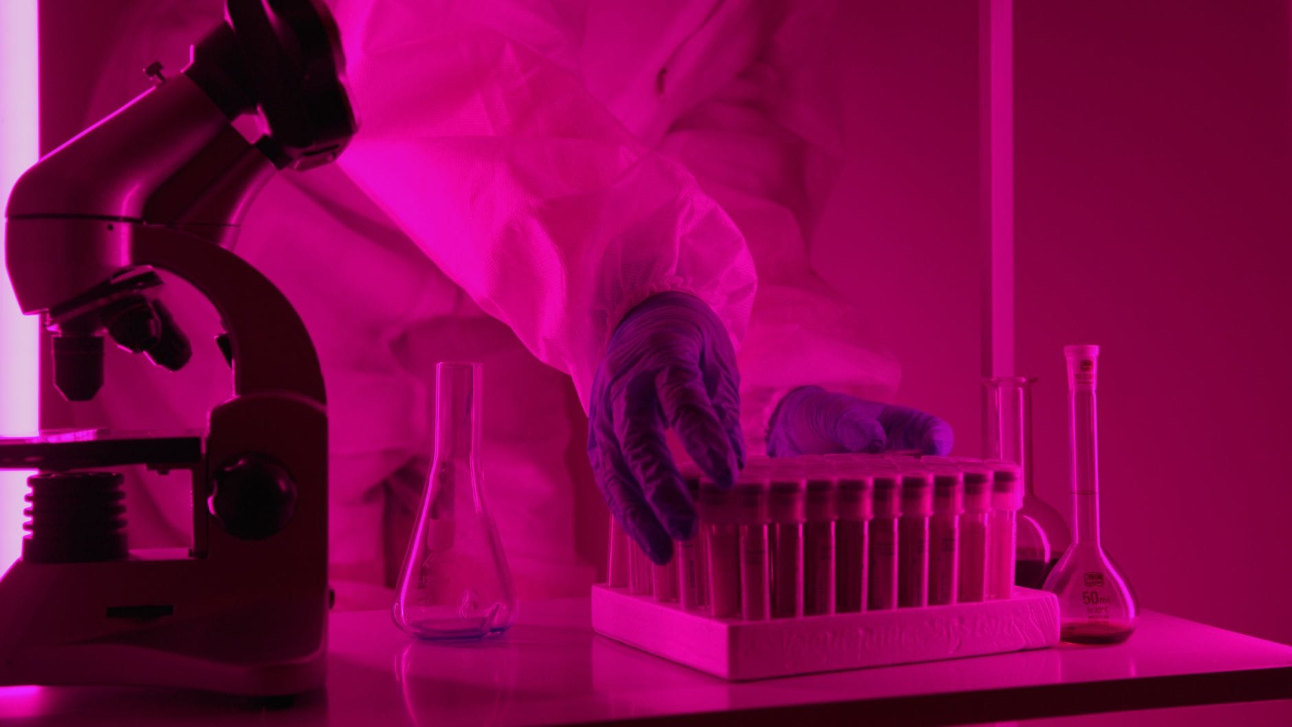 Naukowiec przy mikroskopie i probówkach w laboratorium pod różowym światłem