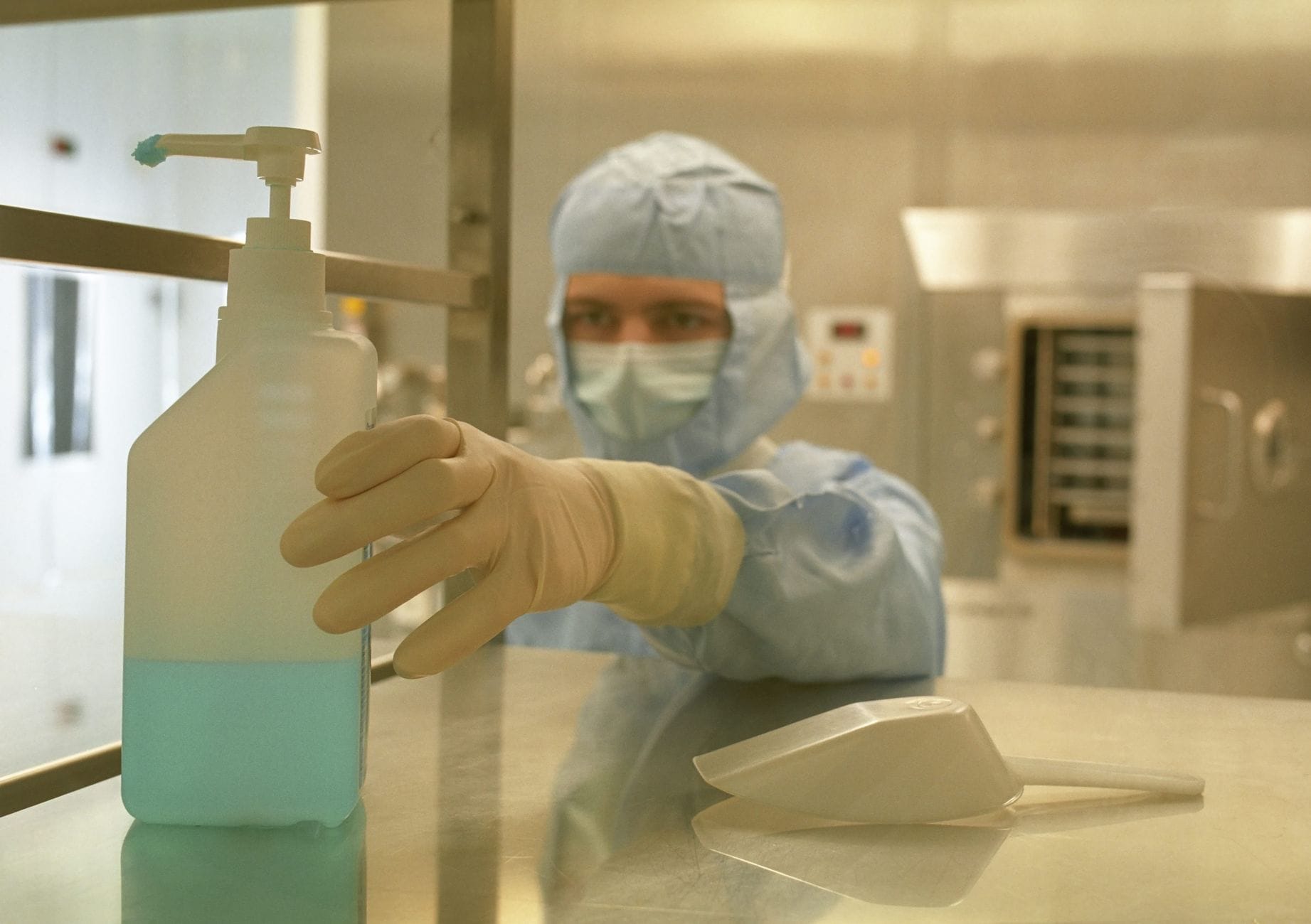 Naukowiec w odzieży ochronnej sięga po środek do dezynfekcji w laboratorium Naukowiec w odzieży ochronnej sięga po środek do dezynfekcji w laboratorium