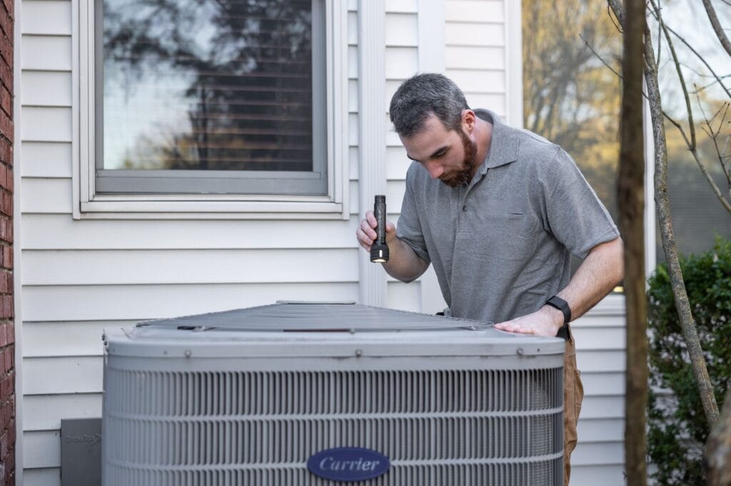 Technik sprawdza zewnętrzną jednostkę HVAC przed sezonem grzewczym